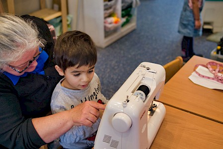 An early years practitioner and a young boy. She is teaching him to use a sewing machine.