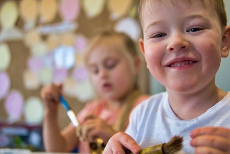 A close up of a young boy who is smiling and holding a paintbrush.