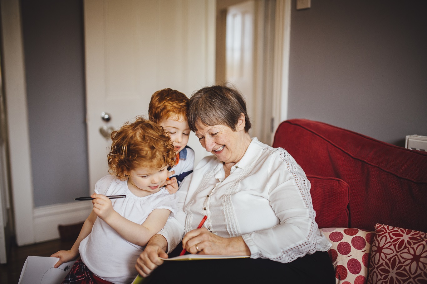 A female childminder draws for two young children in her living room.